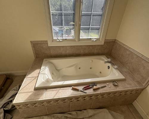 White jetted bathtub with tan tile surround installed beneath a window