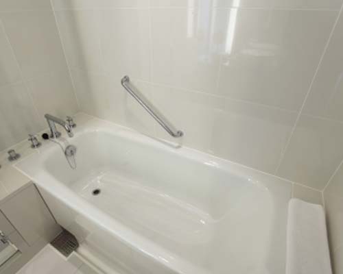 White soaking bathtub with clean white tile surround, chrome fixtures, and grab bar