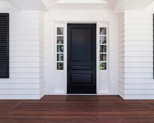 Black front door with white sidelights on white home with wood deck porch
